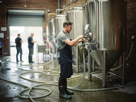 A brewer adjusting a valve on a steel fermenting tank