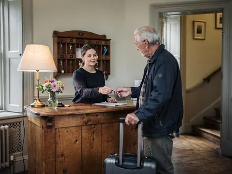A receptionist handing a room key to a guest at a small hotel